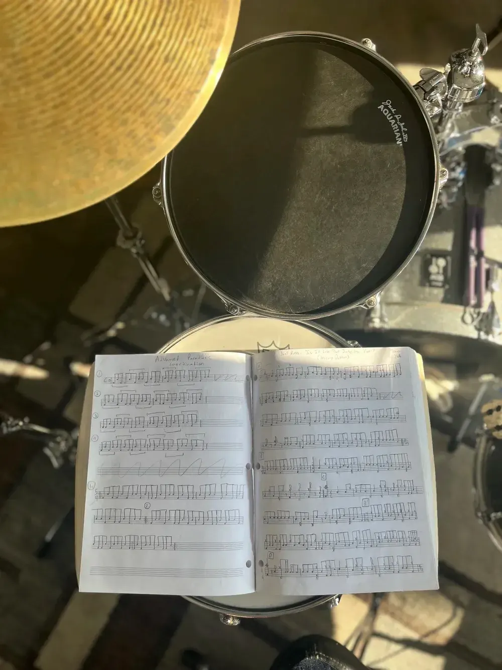 Open notebook of hand-written drum exercises resting on a snare drum